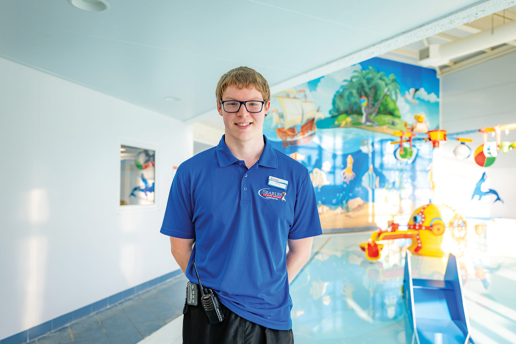 Male student in blue polo top, with a children's splash pool behind 